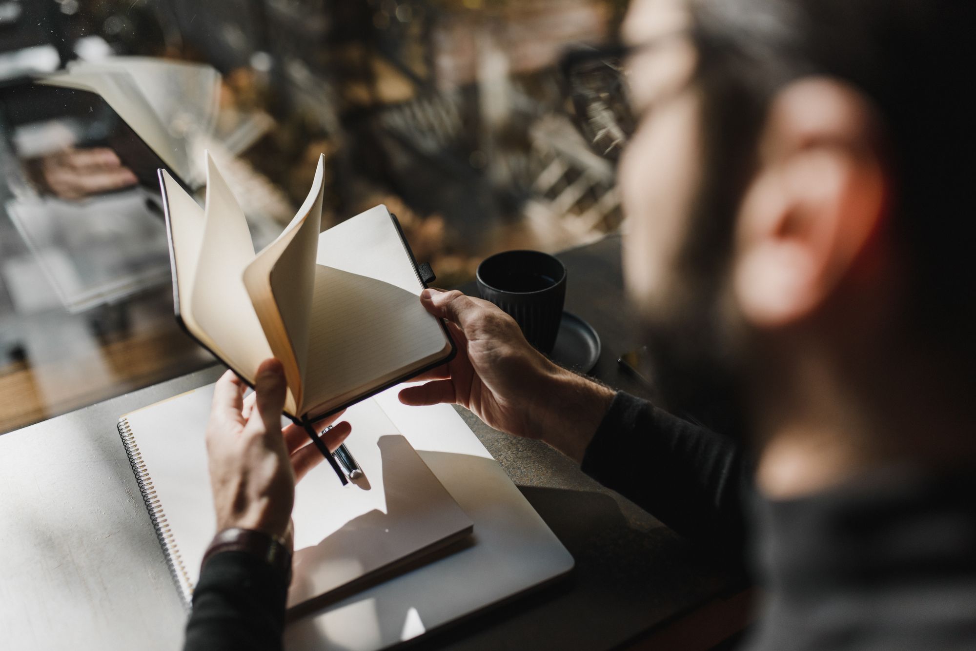 A person turning the pages of a notebook by a window.