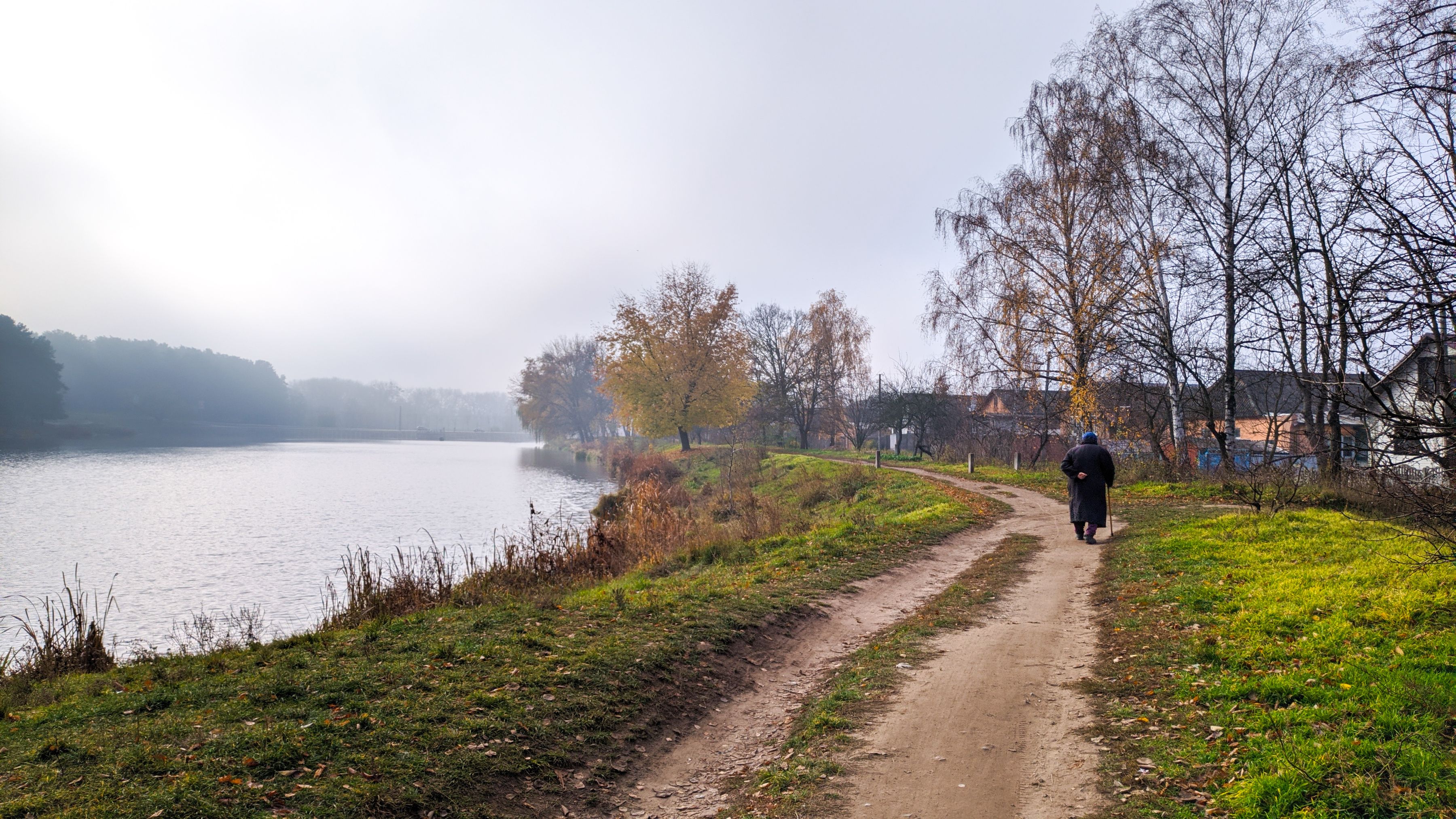 A person walking alone along a riverside path on a quiet morning.